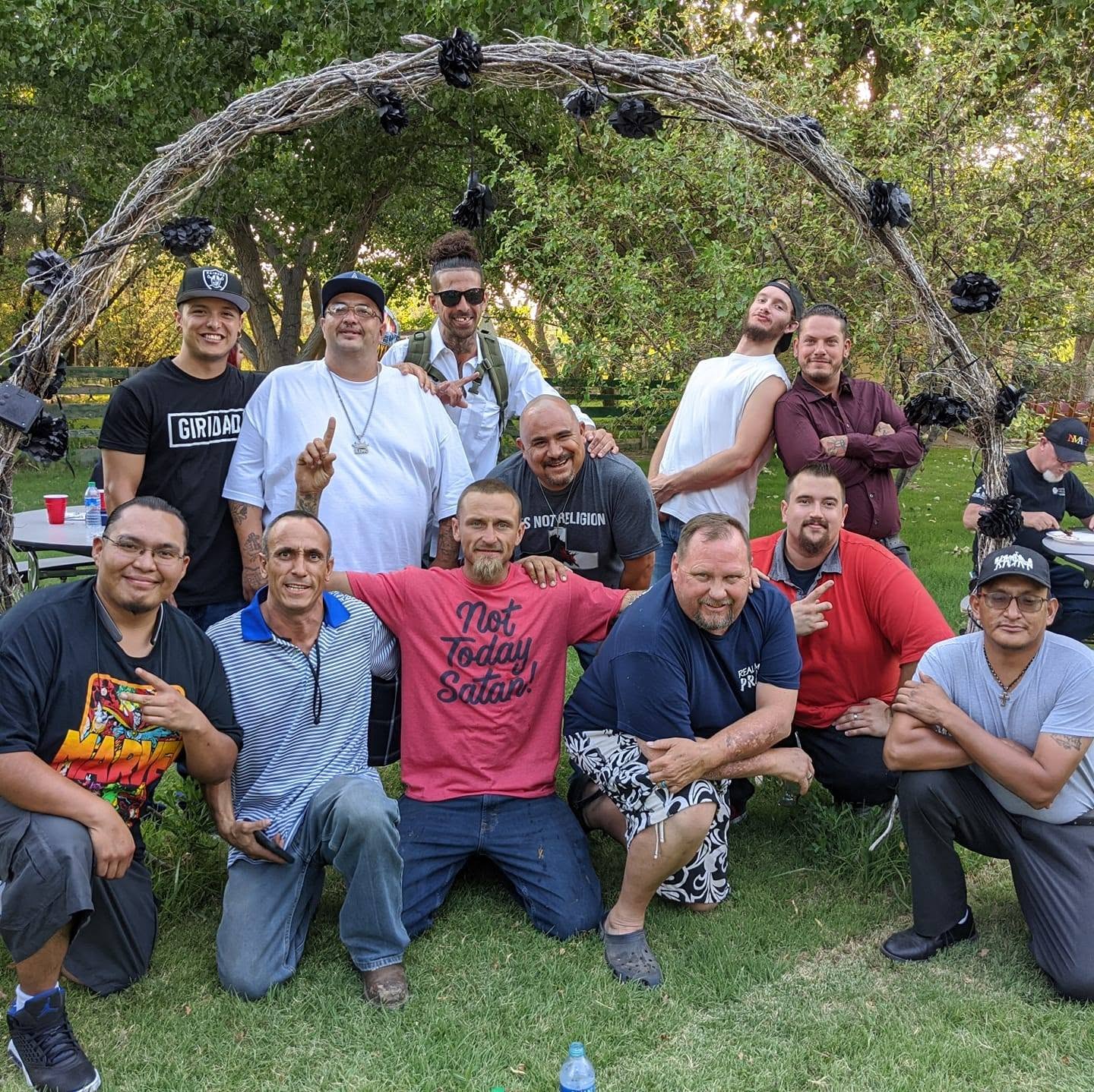 Men of Under HIS Construction gathered outdoors under a decorated arch at The Secret Sanctuary